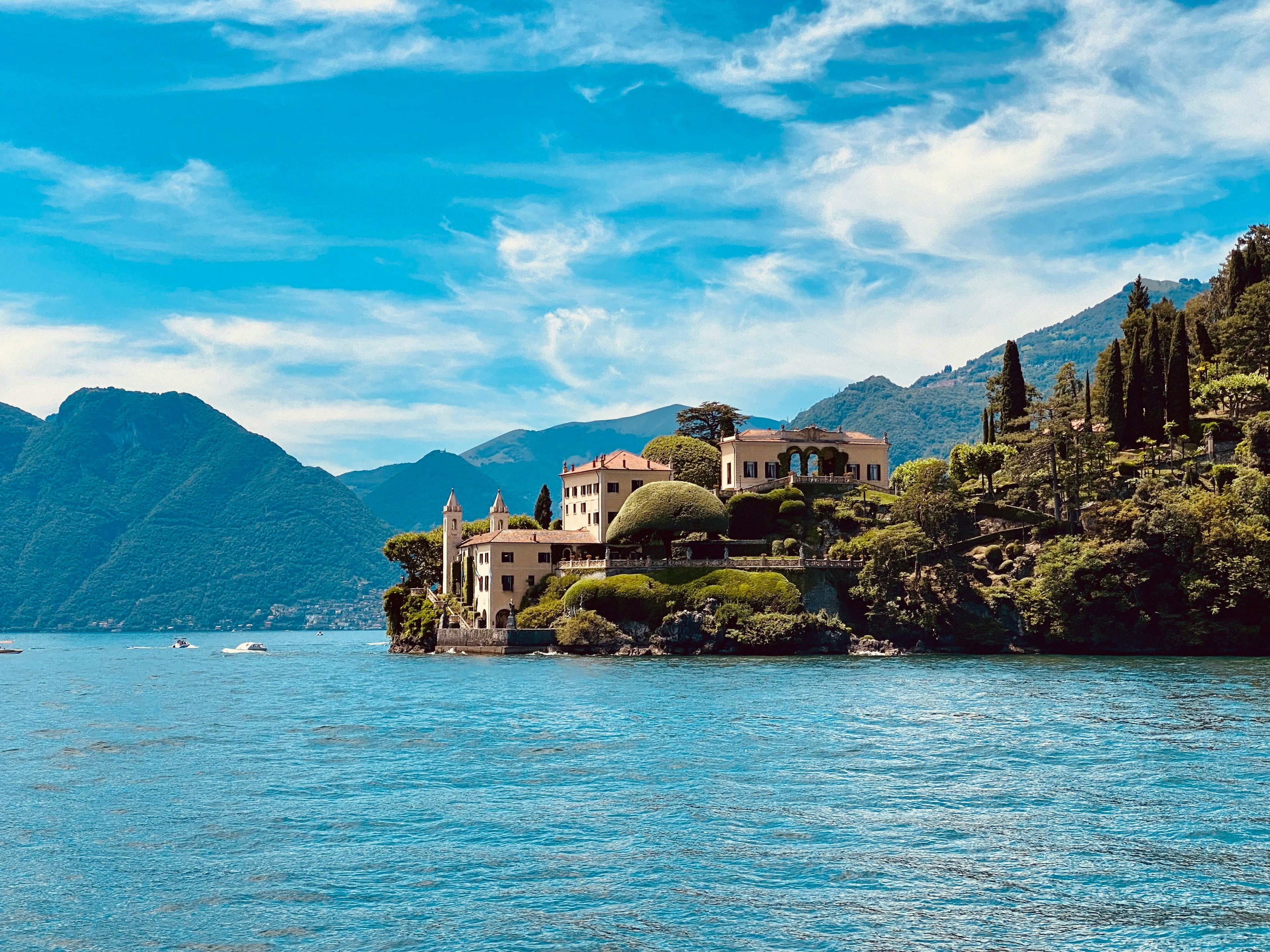 Lake Como view with buildings surrounded by water and mountains under a blue sky