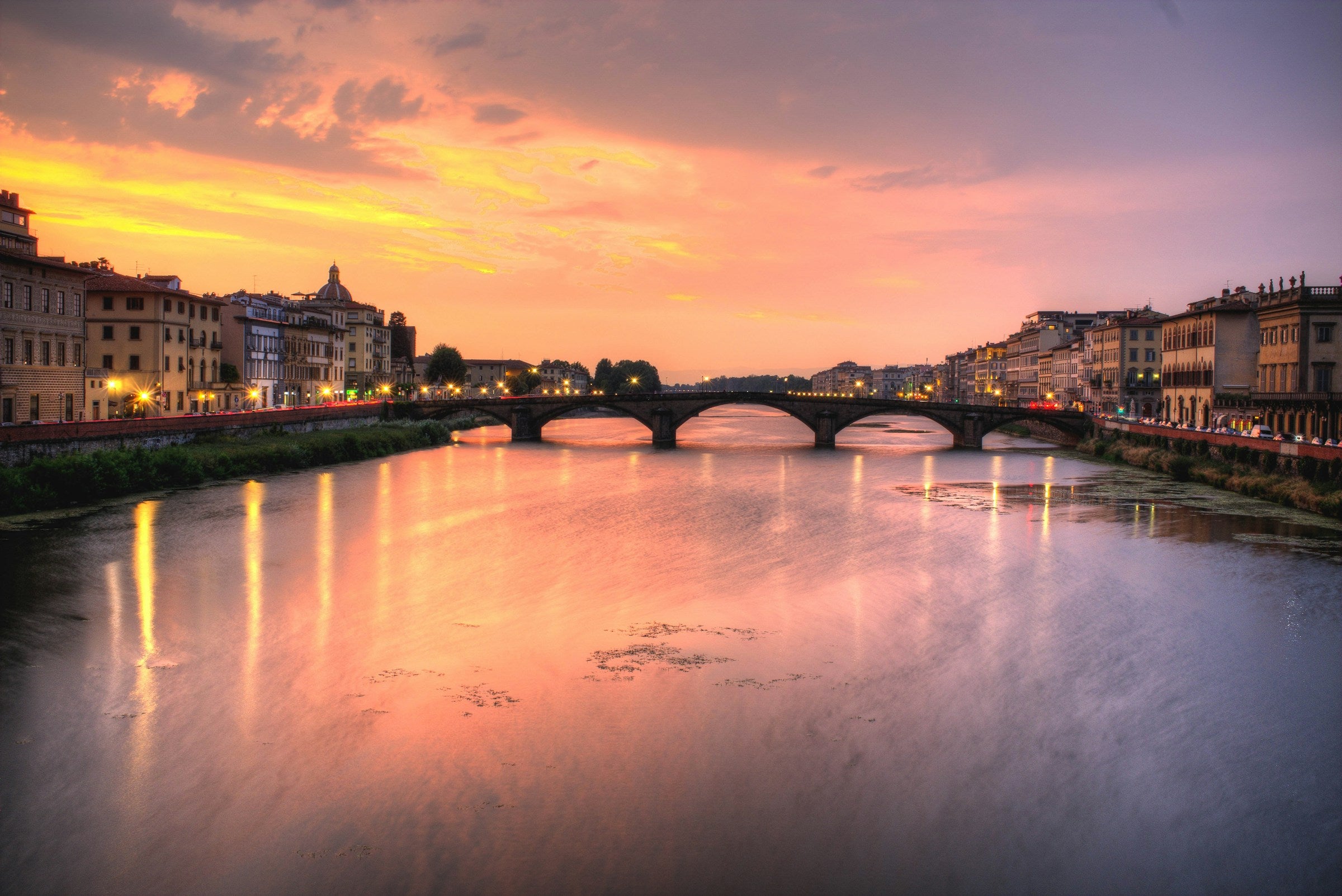 Firenze with a bridge over a river at sunset, with warm colors in the sky.