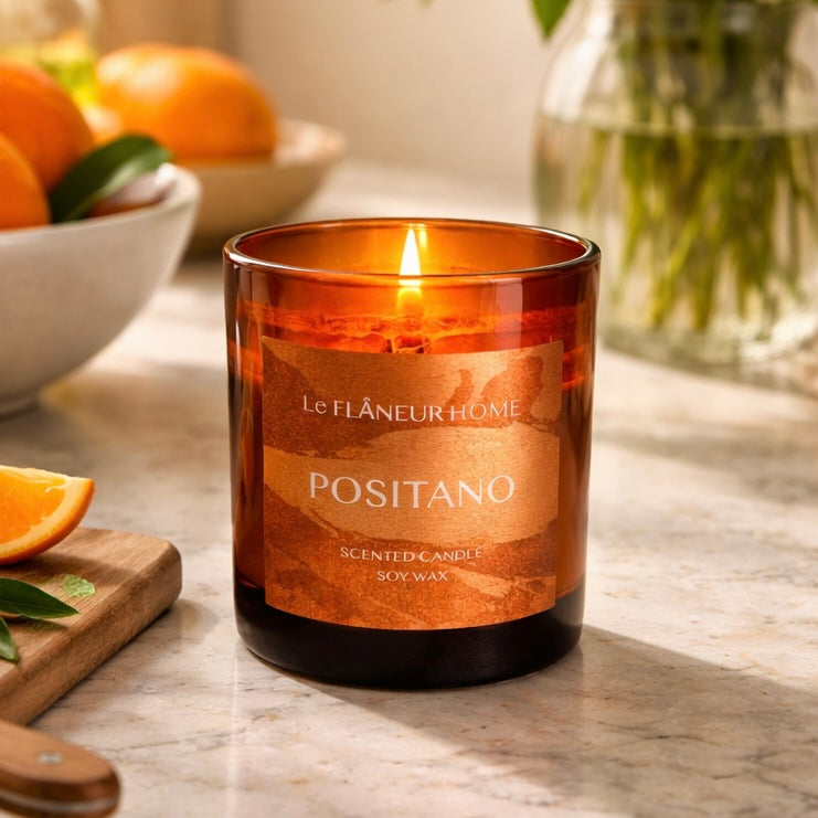 Scented candle labeled 'POSITANO' by Le Flâneur Home on a marble surface with oranges and a cutting board.