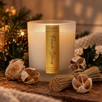 Le Flâneur Home Fireside Stories scented candle in frosted white glass with a gold label, styled with holly and a knitted blanket.